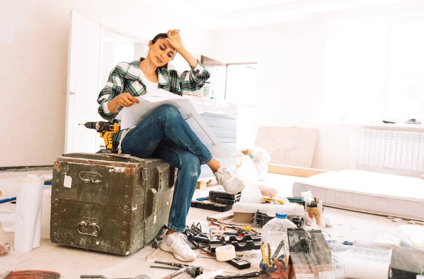 selling a home in North Georgia: Young tired woman with house plan is sitting on box among building materials and inventory. Girl in casual clothes is thinking about home renovation. Brunette dreams of new interior of room.